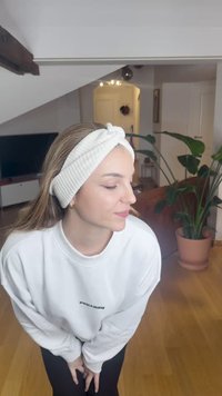 Toucado branco canelado com detalhe de nó, combinado com um sweatshirt branco com o texto "PEZADOR", situado numa sala com plantas e uma televisão.