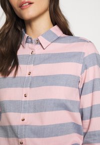 Chemise rayée avec des rayures horizontales alternées rose clair et bleu, fermeture à boutons et col classique. Tissu doux avec une texture lisse.