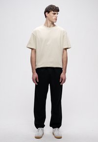 Roomkleurig katoenen t-shirt, met een relaxte pasvorm en korte mouwen, gecombineerd met zwarte joggingbroek en witte sneakers. Neutrale tinten en een eenvoudig ontwerp.