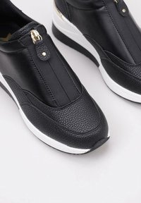 Zapatillas negras con un upper de cuero texturizado, que cuentan con una suela blanca, cierre de cremallera y detalles lisos en la punta y el talón.