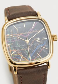 Reloj cuadrado dorado con una esfera temática de mapa negro que presenta líneas coloridas. Correa de cuero marrón con sutiles detalles de costura.