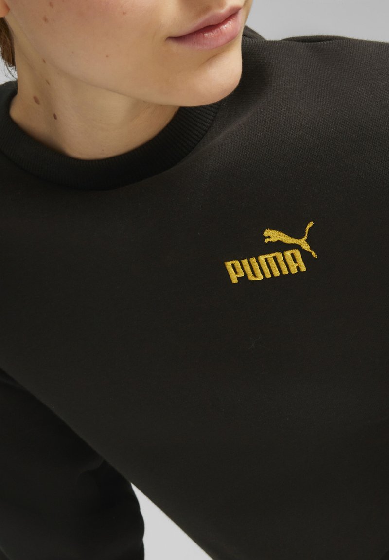 Crna dukserica s okruglim izrezom, s istaknutim žutim izvezenim Puma logotipom na prsima. Glatka tekstura tkanine.