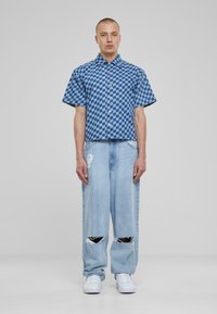 Camicia a maniche corte a quadri blu con bottoni, abbinata a jeans a gamba larga blu chiaro strappati e sneakers bianche.