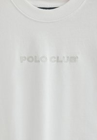 Vit bomull T-shirt med ribbat runt halsringning, med "POLO CLUB" broderat i ljusgrått över bröstet. Enkel och ren design.