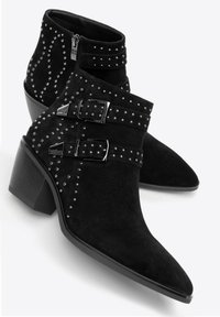 Zwarte suède enkellaarsjes met puntige neuzen, blokhakken, zilveren studs, twee verstelbare riemen met gespen en een ritssluiting aan de zijkant.