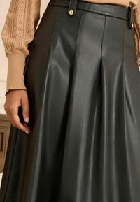 Fekete műbőr szoknya redőkkel, szűkített derékkal és arany gombos díszítéssel. Simás textúra és légies dizájn.