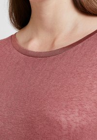 T-shirt a maniche corte e collo rotondo in colore rosa sbiadito, con scollo a costine e tessuto leggero e testurizzato.