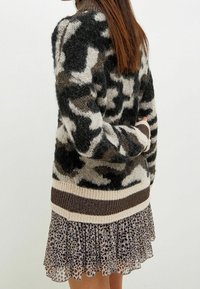 Maglione lavorato a maglia in tonalità di nero, beige e marrone con un motivo astratto, dettagli a costine e un vestito a pois trasparente a strati.
