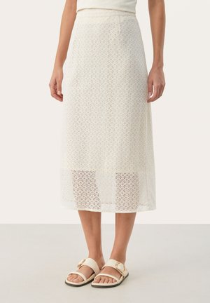 Jupe en dentelle crème avec un motif floral et une finition texturée ; longueur genou avec un ourlet transparent. Associée à des sandales beiges avec une boucle dorée.