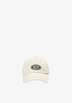 Gorra de béisbol beige con visera curva que presenta un parche ovalado verde oscuro y letras blancas "SCP" centradas en el panel frontal.