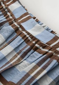 Gros plan d'un tissu froncé avec un motif à carreaux bleu, marron et blanc, et une ceinture élastique cousue, sur un fond clair.
