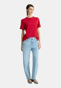 T-shirt rosso a maniche corte abbinato a jeans a gamba dritta blu chiaro e ballerine in bianco e nero con motivo, che presenta una vestibilità casual e un design semplice.