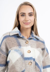 Gecontroleerde wollen shirtjacket in beige, witte en blauwe tinten. Voorzien van een knoopsluiting aan de voorkant, een kraag en twee voorzakken met ronde hoeken.