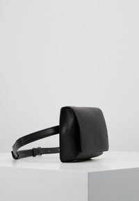 Borsa in pelle nera con forma rettangolare, chiusura a pattina piatta e tracolla regolabile. Texture liscia con dettagli hardware minimi.