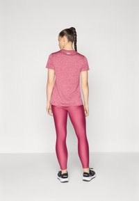 Czerwony, melanżowy T-shirt sportowy z krótkimi rękawami, zestawiony z błyszczącymi, obcisłymi bordowymi legginsami. Obuwie: czarne buty biegowe z białymi podeszwami.