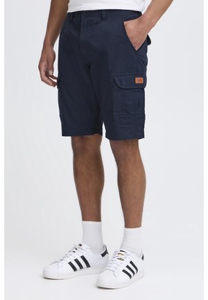 Marine-farbene Cargo-Shorts aus Baumwolle mit zwei seitlichen Taschen und einem Patch-Label, kombiniert mit weißen Sneakers mit schwarzen Streifen und gerippten Socken.