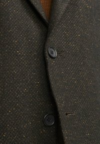 Giacca in tessuto color marrone con una leggera spruzzata dorata, dotata di due bottoni neri e un design con revers a punta.