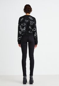 Fekete pulóver fehér masni mintákkal, fekete skinny farmernadrággal és fekete bokacsizmával párosítva; texturált kötött anyag.