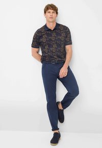 Marineblaues kurzärmeliges Polohemd mit floralem Muster, kombiniert mit marineblauen Chinos und dunklen Sneakern. Verfügt über einen klassischen Kragen und einen strukturierten Stoff.