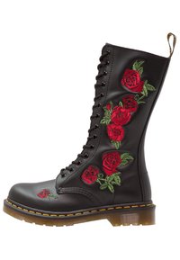 Bottine en cuir noir avec des roses rouges brodées, bout rond, lacets et surpiqûres jaunes le long de la semelle. Semelle extérieure en caoutchouc transparent et striée.