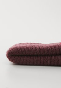 Foldet maroon ribbet strikstof, set tæt på på en ensfarvet lys grå baggrund.
