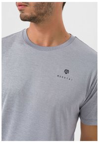 Grå kortærmet t-shirt lavet af blødt stof, med rund halsudskæring og et sort logo på venstre brystområde.