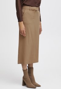 Een beige midi-jurk met een slim fit, voorzien van zijzakken en schone naden. Gepaard met nauwsluitende, kniehoge bruine enkellaarsjes.