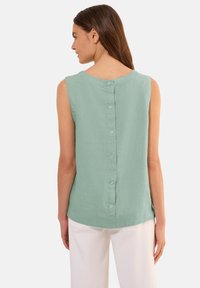 Hellgrünes ärmelloses Blusenshirt aus weichem Stoff, mit rundem Halsausschnitt und Knopfverschluss am Rücken. Schlichtes, unverziertes Design.