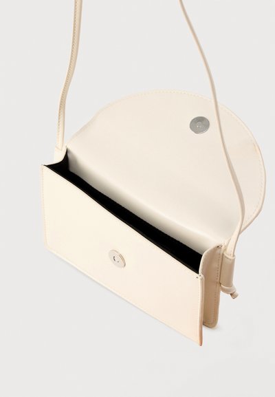 Μικρή μπεζ δερμάτινη τσάντα χιαστί με μαγνητικό κούμπωμα, ανοιχτή για να δείχνει έναν εσωτερικό χώρο και λεπτό ιμάντα ώμου.