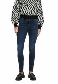 Vaqueros ajustados en denim azul oscuro con costuras en contraste, combinados con un suéter estampado en blanco y negro y mocasines negros.