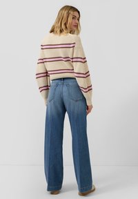 Sweter dziany w kremowym kolorze z różowymi i brązowymi paskami, zestawiony z niebieskimi, szerokimi spodniami z wysokim stanem. Gładkie faktury, luźny krój.