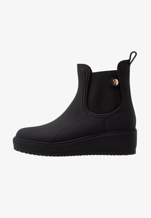Botas de tobillo de goma negra con un diseño elegante, paneles laterales elásticos, punta redonda y tacón de cuña, con un acento de logo metálico.