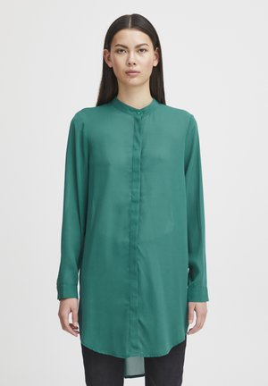 Long-sleeve, button-up shirt in solid emerald green, made of smooth fabric with a high collar and a slightly curved hem.