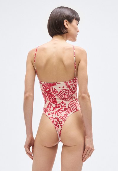 Bañador de una pieza en crema claro con estampado de texto abstracto en rojo. Presenta tirantes delgados y un corte atrevido, resaltando una textura suave.