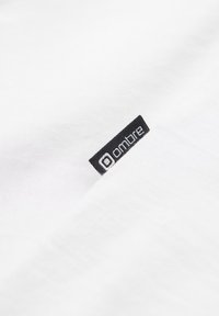 Weißes Baumwoll-T-Shirt mit gerippter Textur, mit einem schwarzen Etikett mit dem Text "ombre" am unteren Rand.