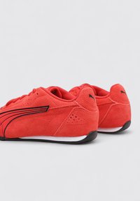 Baskets sportives en daim rouge avec une texture lisse, une semelle blanche et des accents noirs le long des côtés et du logo. Design bas.