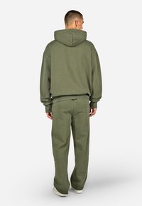 Felpa verde oliva con cappuccio regolabile e polsini a coste, abbinata a pantaloni larghi coordinati. Tessuto morbido e testurizzato. Design minimalista.