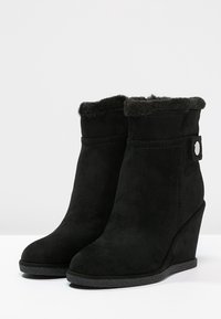 Bottines à talon compensé en suède noir avec un col en fourrure douce et un détail de bouton décoratif. Semelle en caoutchouc texturé pour une meilleure adhérence.