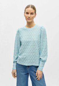 Lys blå, langermet topp laget av teksturert blonde med blomstermønster og rund hals. Loose passform med lett puffede skuldre.