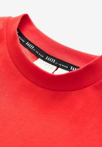 Camiseta de algodón roja con cuello redondo. Presenta una etiqueta negra en el interior con "BAKER by Ted Baker" en texto blanco. Textura suave.