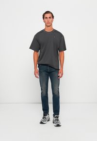 Grå t-skjorte med korte ermer og rund hals, kombinert med blå jeans og svart-hvite sneakers. Slim fit, glatt tekstur, minimal branding.