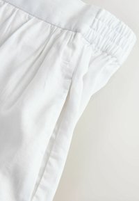 Weiße Hosen mit elastischem Bund und Seitentasche aus leichtem, leicht strukturiertem Stoff.