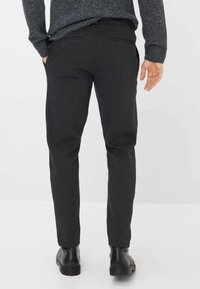 Donkergrijze broek met een slanke pasvorm, gestructureerde stof en twee achterzakken. Draagt een zwarte laars voor extra contrast.