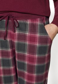 Geruite pyjamabroek in tinten bordeaux en grijs, met een trekkoord in de taille en zijzakken. Zachte stof met een geruite patroon.