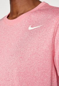 Camiseta deportiva rosa hecha de tela texturizada con escote redondo. Presenta un logo de Nike en blanco impreso en el lado izquierdo del pecho.