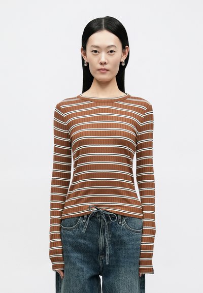 Camisola de malha castanha de mangas compridas com riscas horizontais brancas, decote redondo e corte justo, combinada com jeans de ganga soltos.