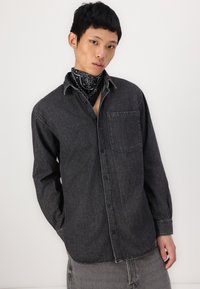 Black denim button-up shirt with a chest pocket, long sleeves, and contrasting stitching details, worn over gray pants with frayed hem.