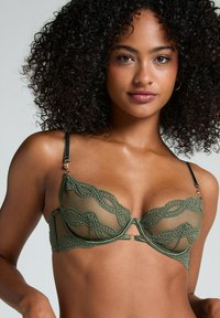 Grøn gennemsigtig bh med blomsterlacemønster, underwire støtte, justerbare sorte stropper og en dekorativ central udskæringsdetalje.