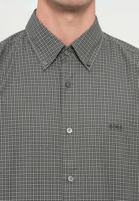 Férfi fekete-fehér, apró kockás, gombos ingben, hegyes gallérral és "BOSS" logóval a mellkasán.