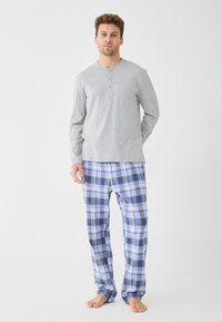 Šedá košeľa s dlhým rukávom a gombíkovou légou, kombinovaná s modro-bielymi károvanými pyžamovými nohavicami. Materiál vyzerá mäkko a ľahko.